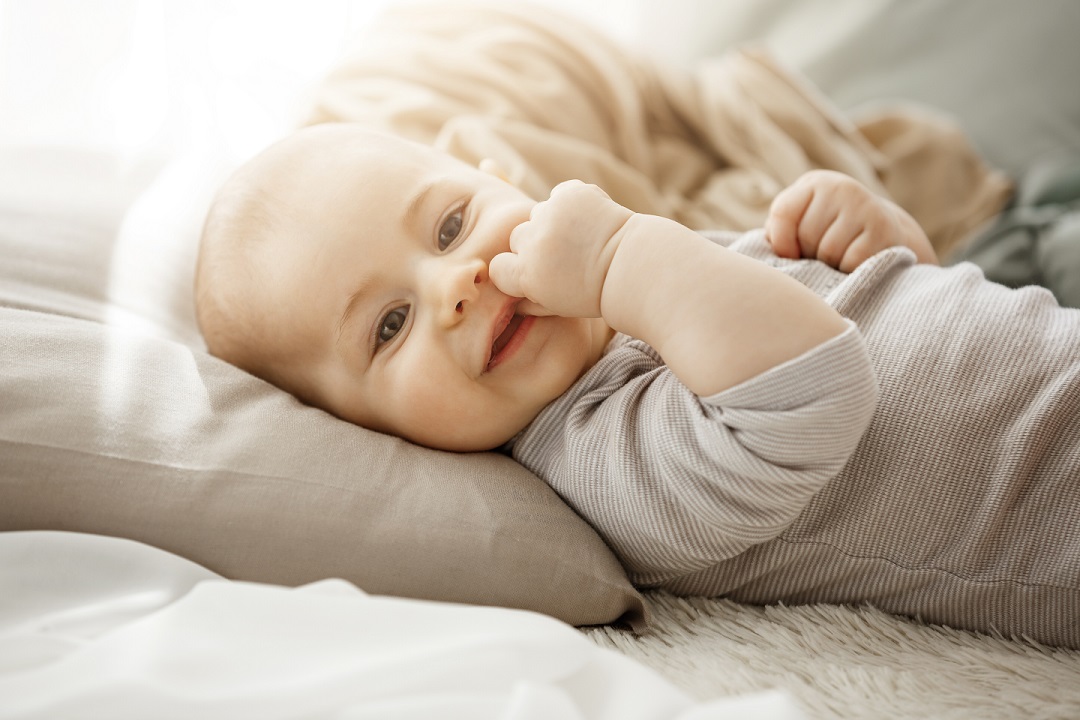 Portrait of sweet smiling newborn daughter. Child looks at camera and touching face with her little hands. Childhood moments